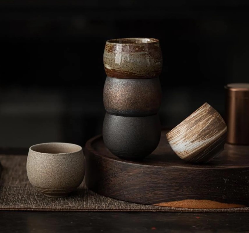 Stacked stoneware tea cups with brushed glazes on a dark wooden tray