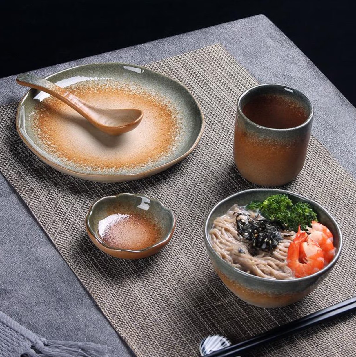 Ochre and grey stoneware noodle bowl, plate, cup and spoon on a woven placemat